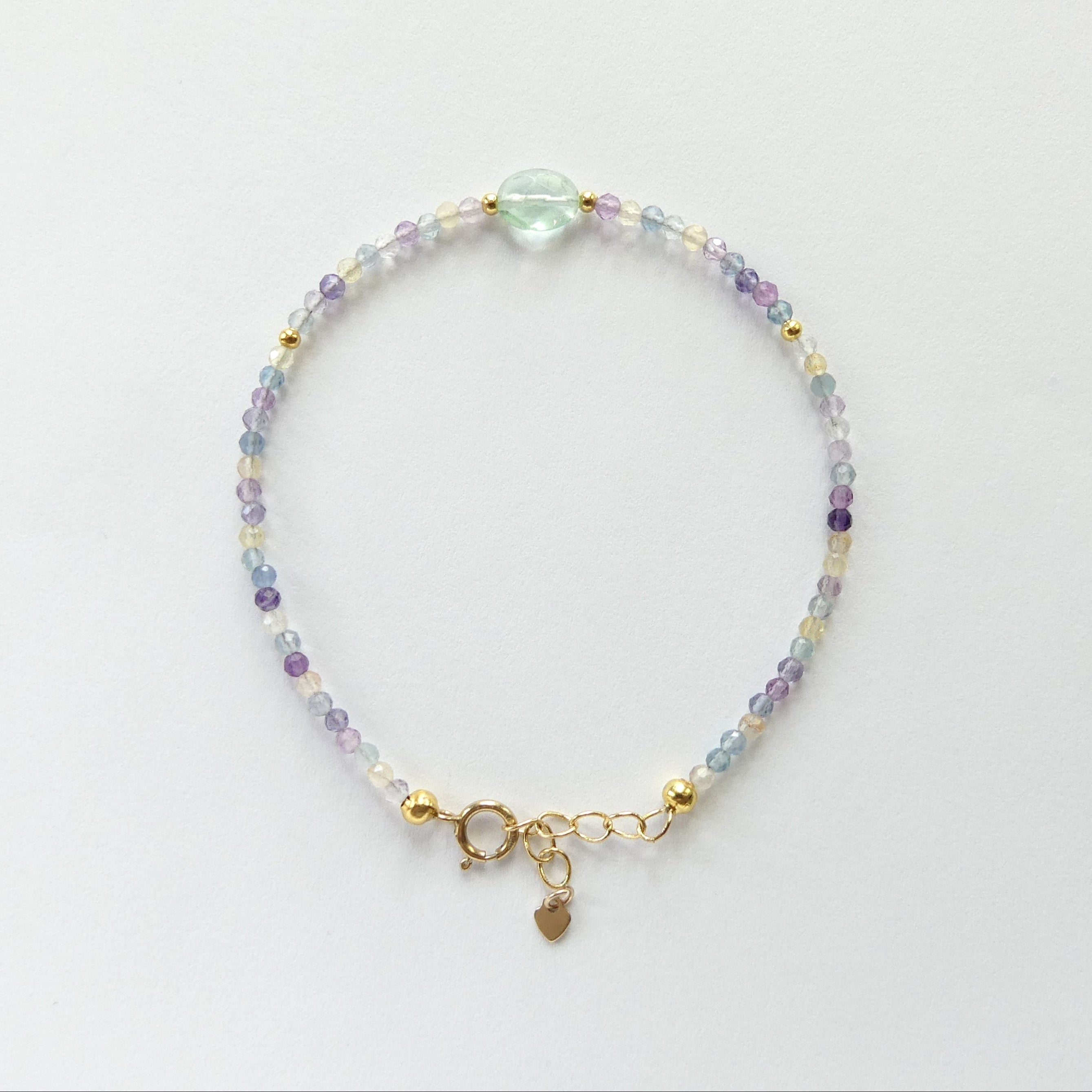 Multicolored beaded dainty fluorite bracelet with a gold clasp on a light gray background
