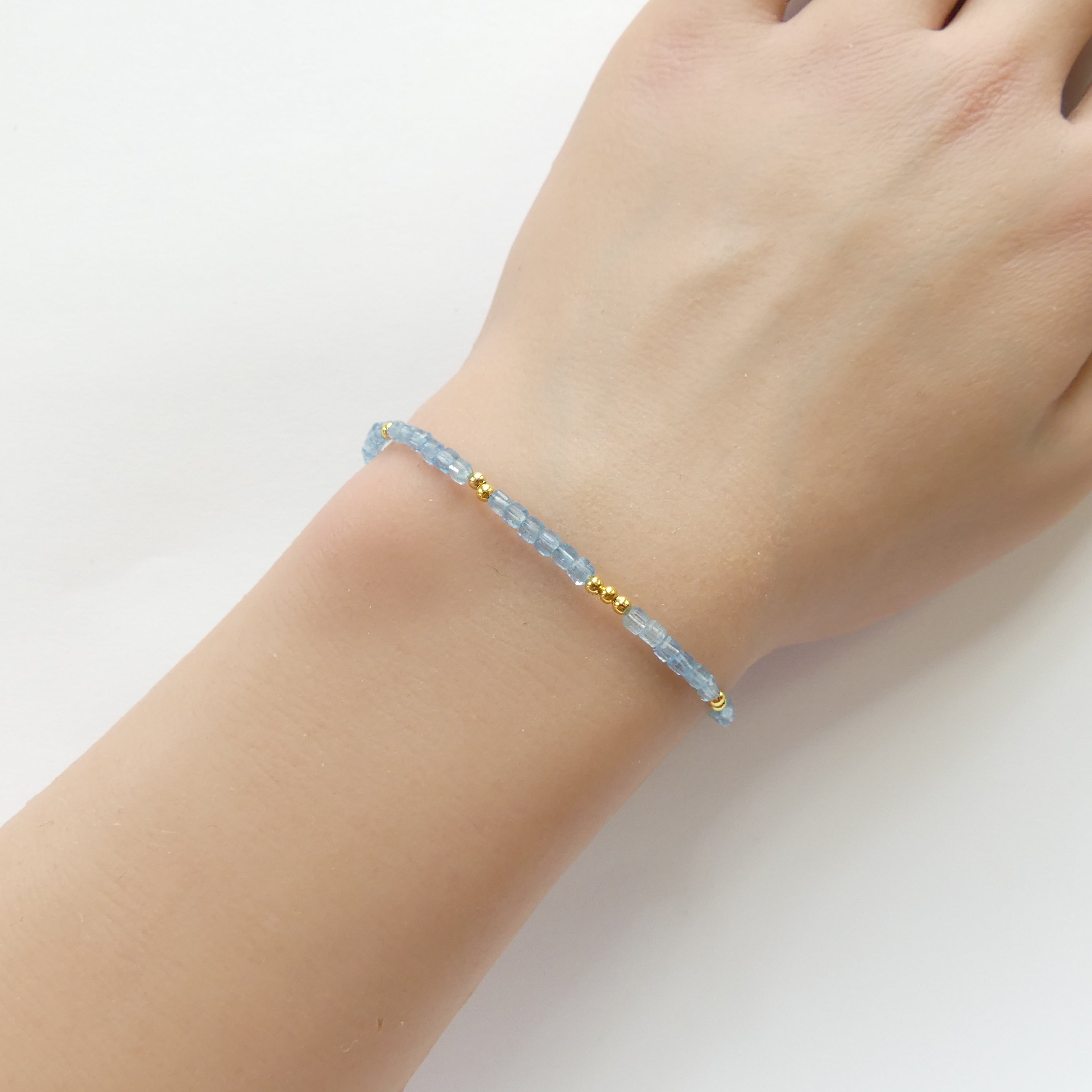 Hand wearing a bracelet santa maria aquamarine tiny dainty bracelet with blue beads on a white background