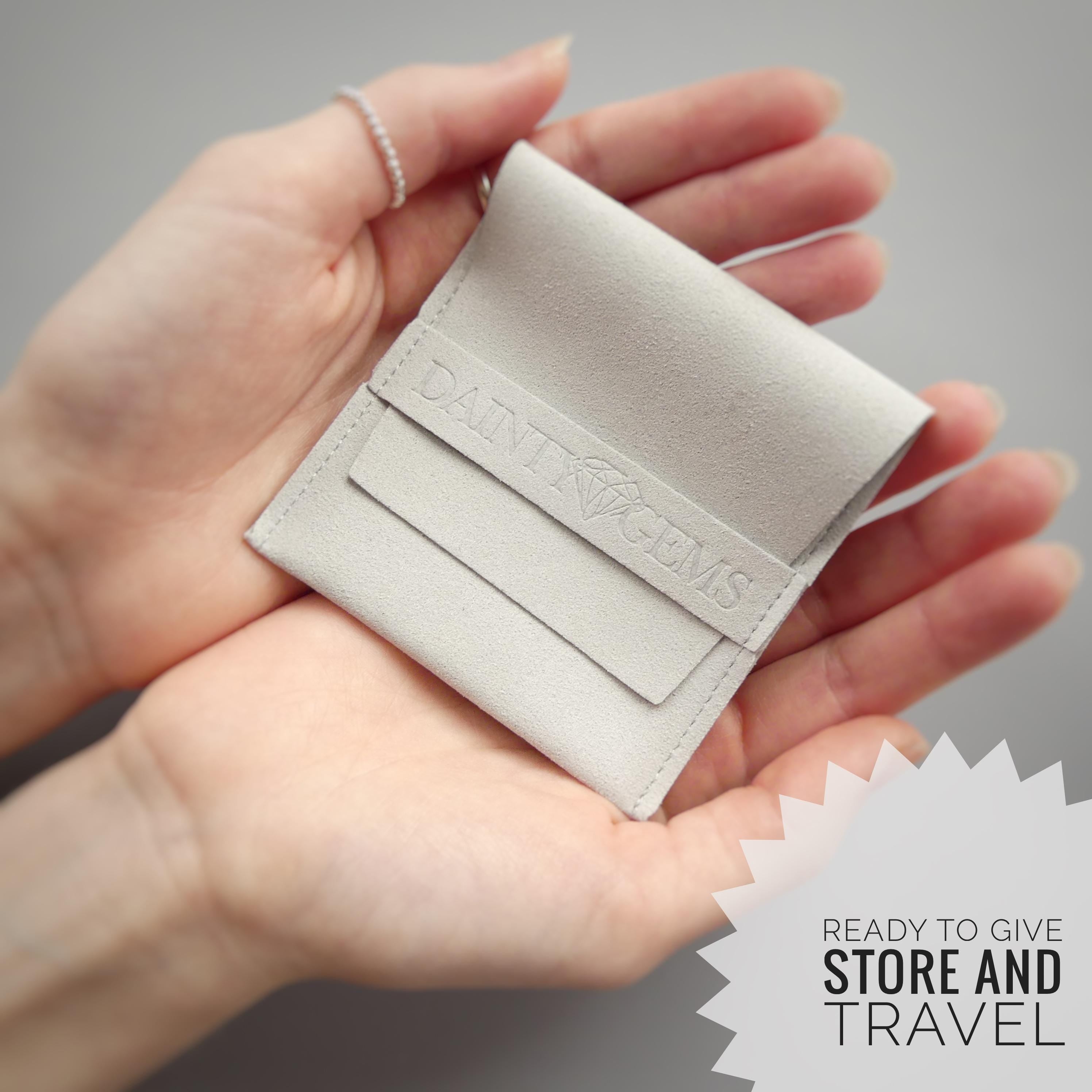A person&#39;s hands holding a small, gray leather pouch with the text &quot;DAINI GEMS&quot; printed on it.