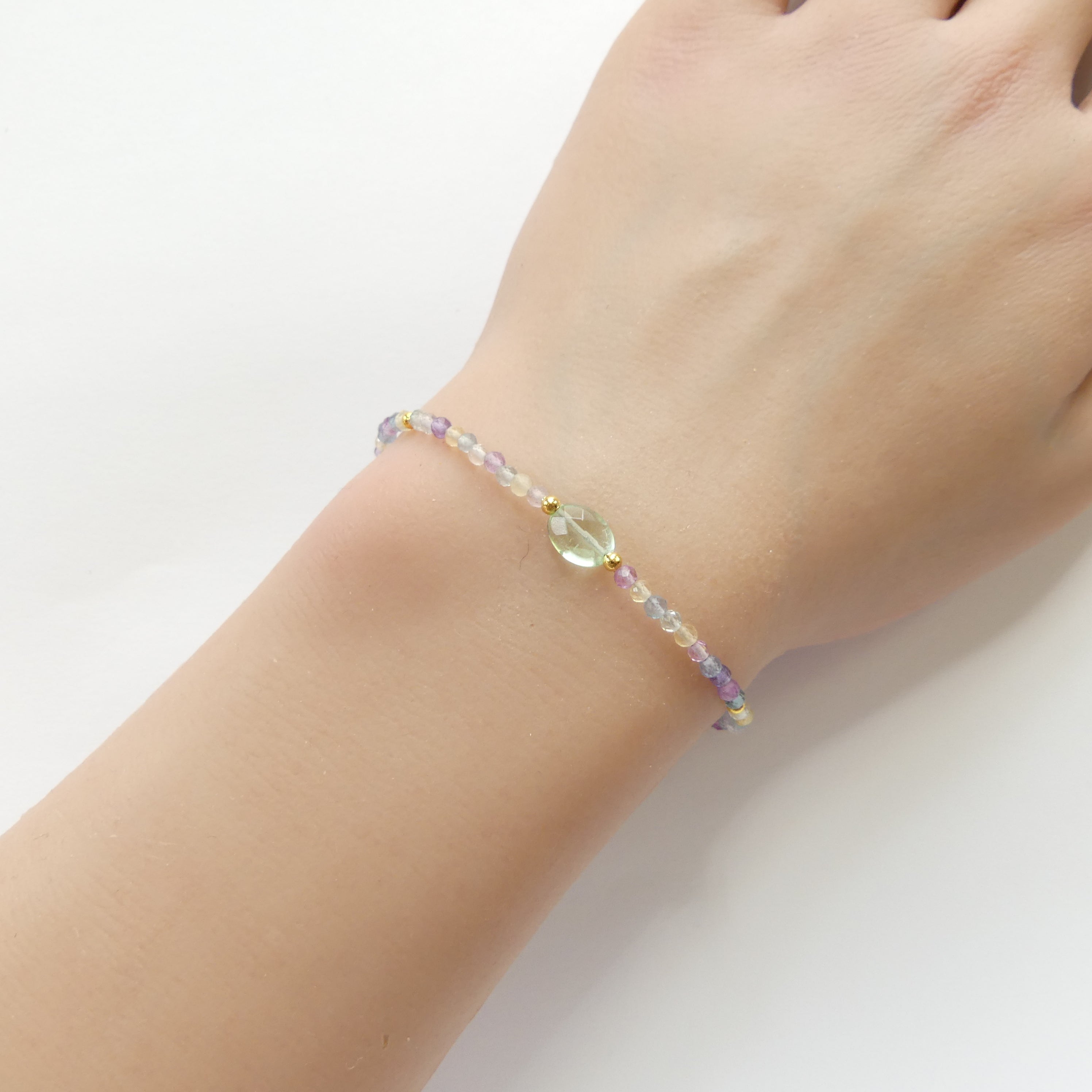 Multicolored beaded fluorite dainty bracelet on a wrist against a white background